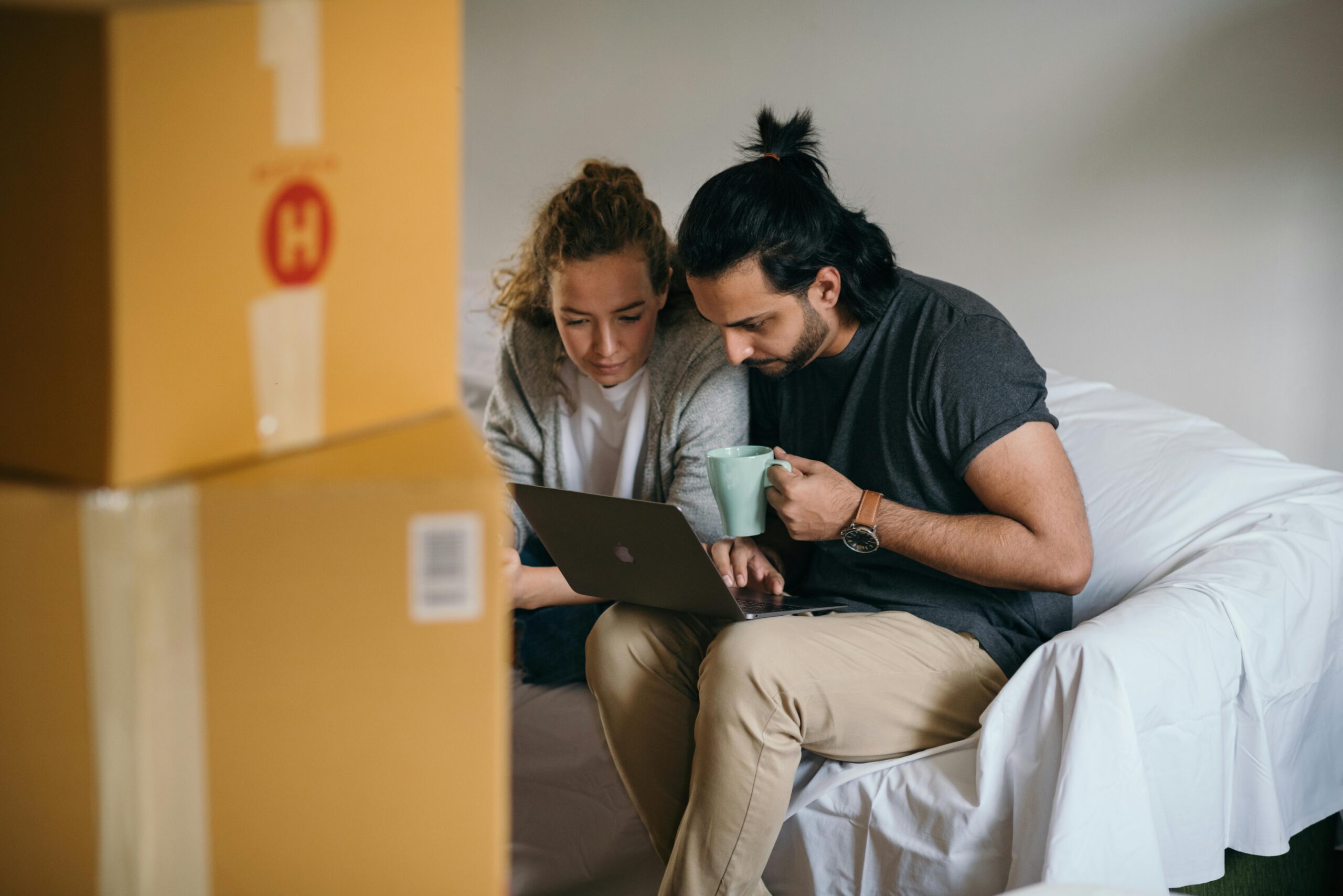 a couple looks at a laptop in a room full of packed boxes.